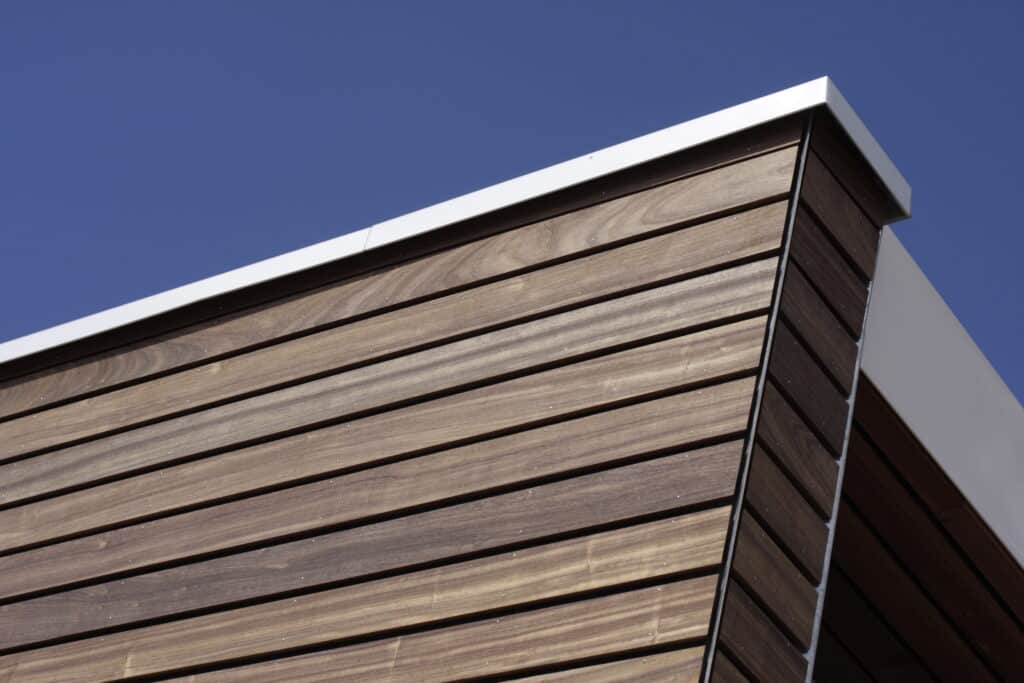 Façade moderne en bois lambrissé avec des clins bruns foncés et des fixations claires, sous une garniture blanche et un ciel bleu.